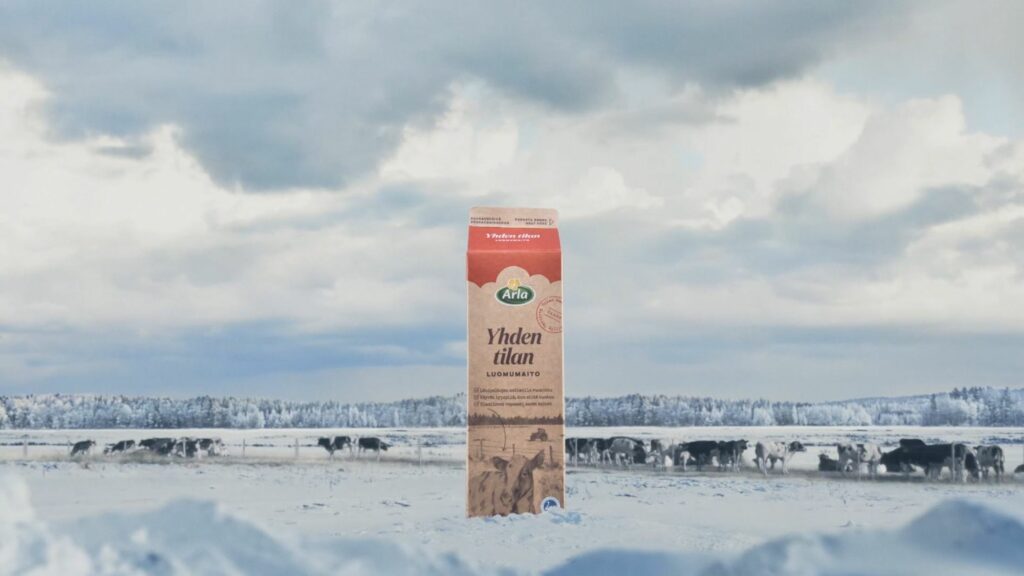 Arla Yhden tilan luomumaitopurkki seisoo lumessa talvipäivänä. Taustalla lehmiä talvisella laitumella.