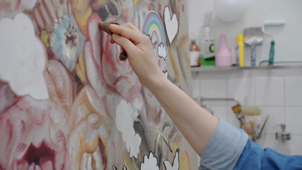 Käsi maalamassa sormiväreillä värikästä taulua jossa kukkia ja sateenkaari.